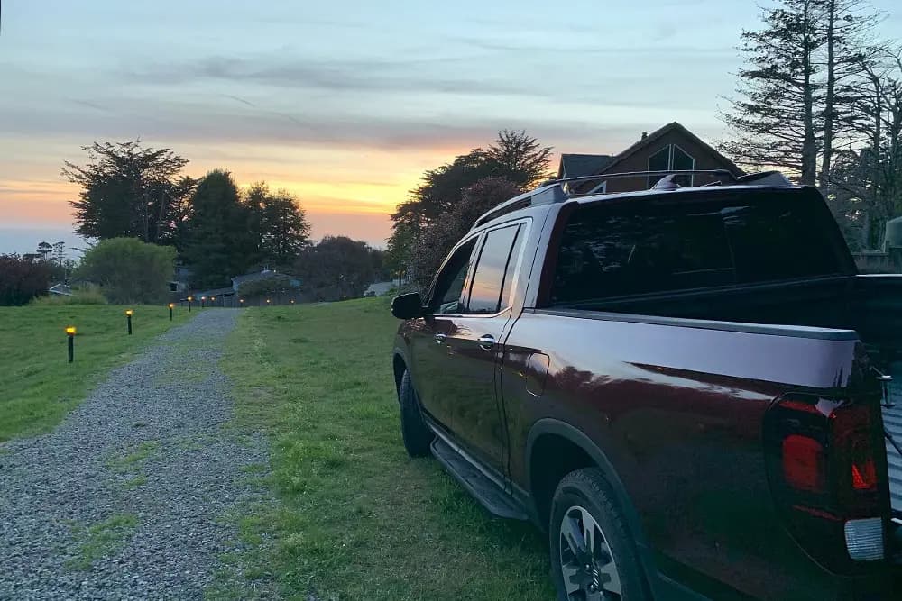 A dark pickup truck parked on a gravel path beside a grassy area at sunset.