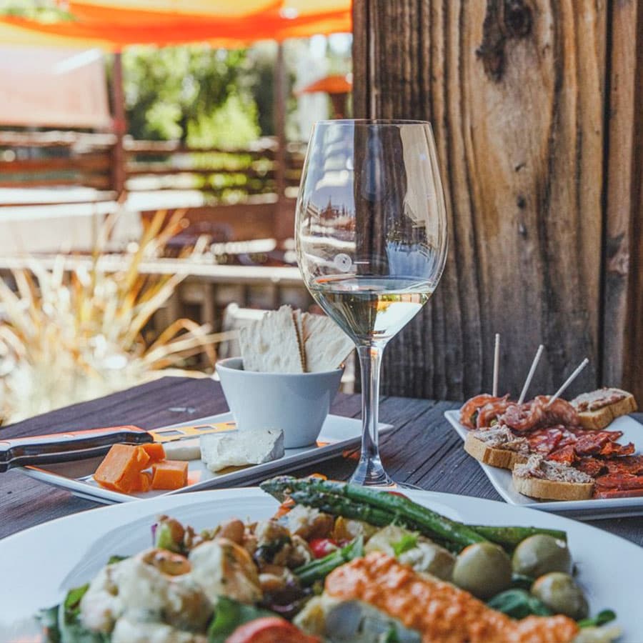 A glass of white wine paired with a charcuterie board and a colorful salad.