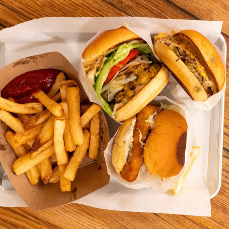A top-down view of a cheeseburger, a double cheeseburger, a fish sandwich, and a side of french fries on a tray.