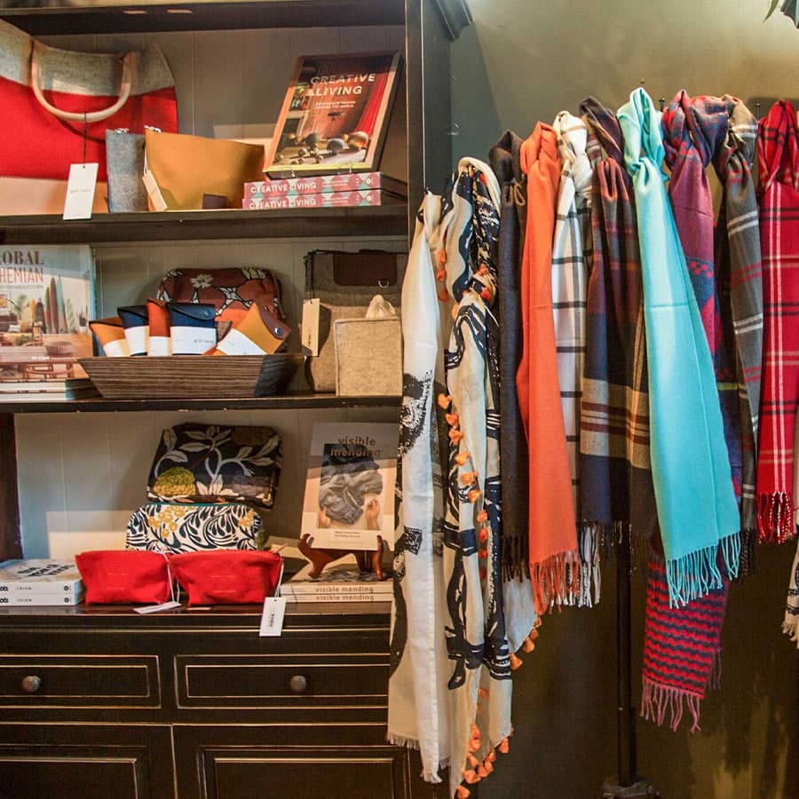 A variety of colorful scarves hanging from a rack, with books and other items on a shelf in the background.