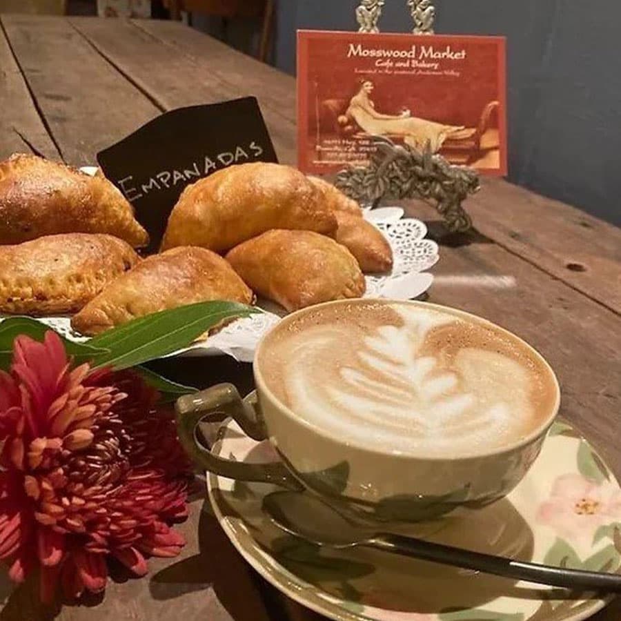 A plate of freshly baked empanadas with a cup of frothy cappuccino.