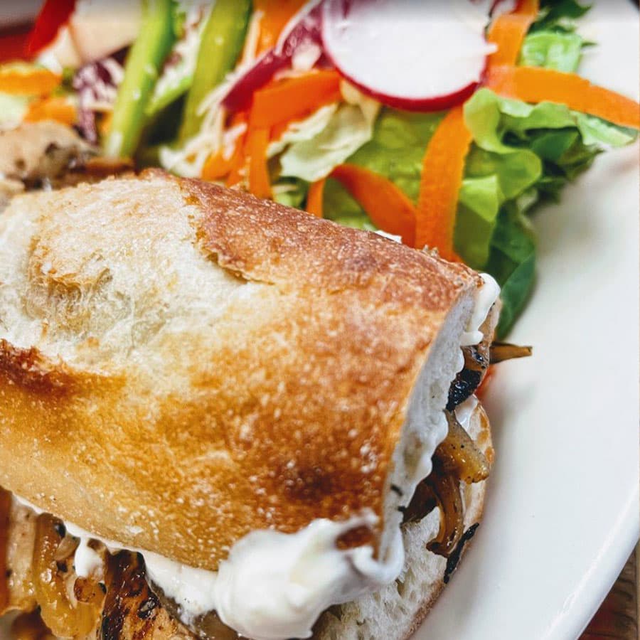 A grilled chicken sandwich on a baguette with a side salad.