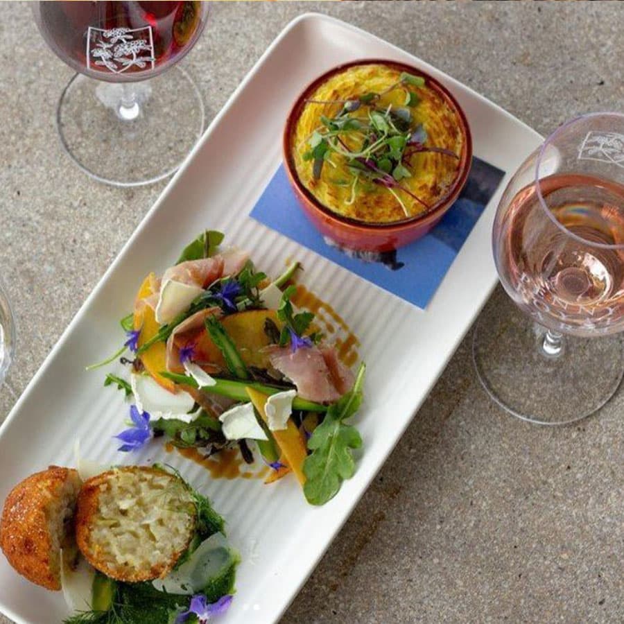 A gourmet meal featuring a salad, arancini, and a baked dish, paired with glasses of red and rose wine.