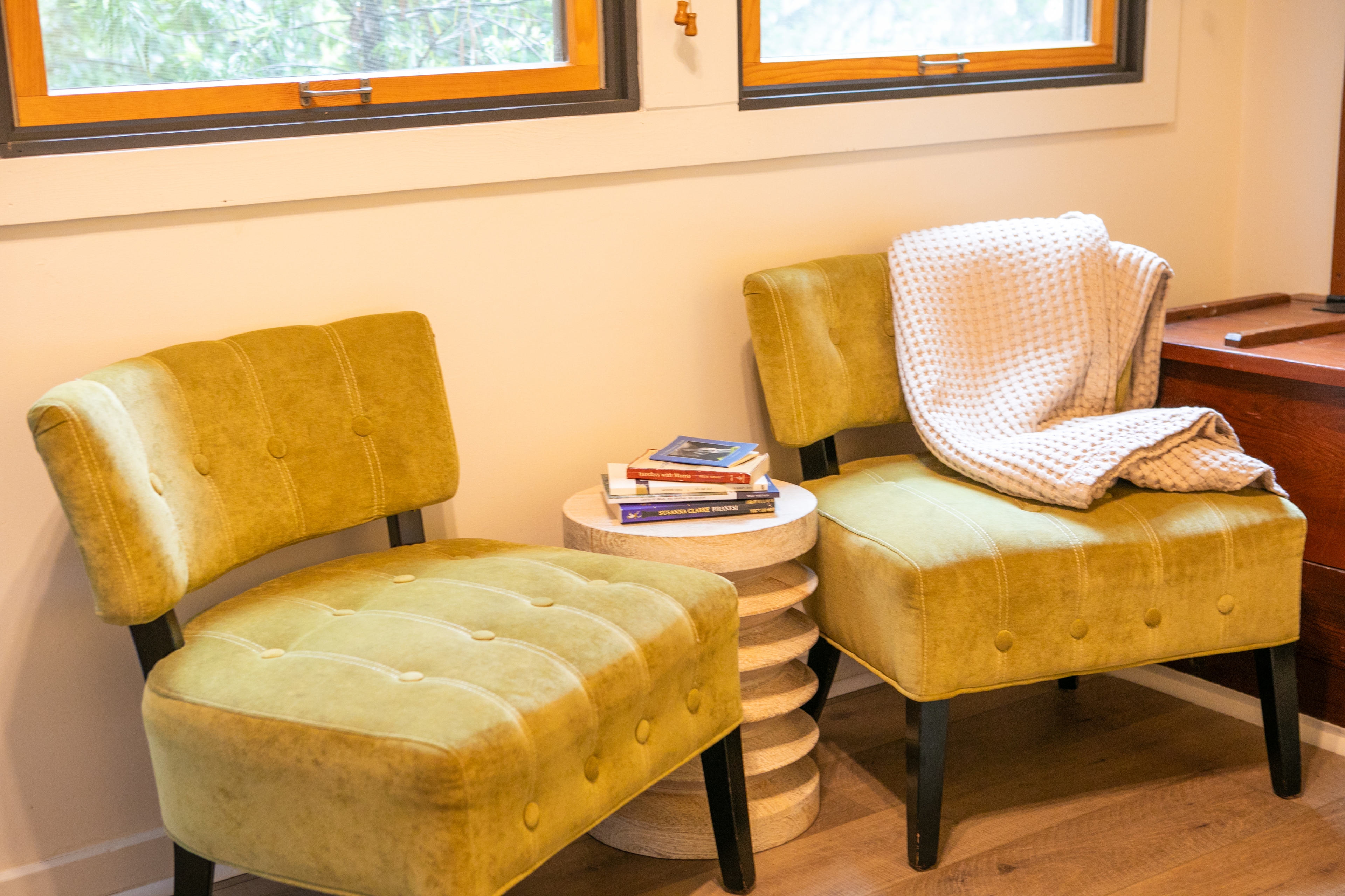 Two yellow chairs with a small round table in between, with a stack of books on the table and a white blanket on one of the chairs.