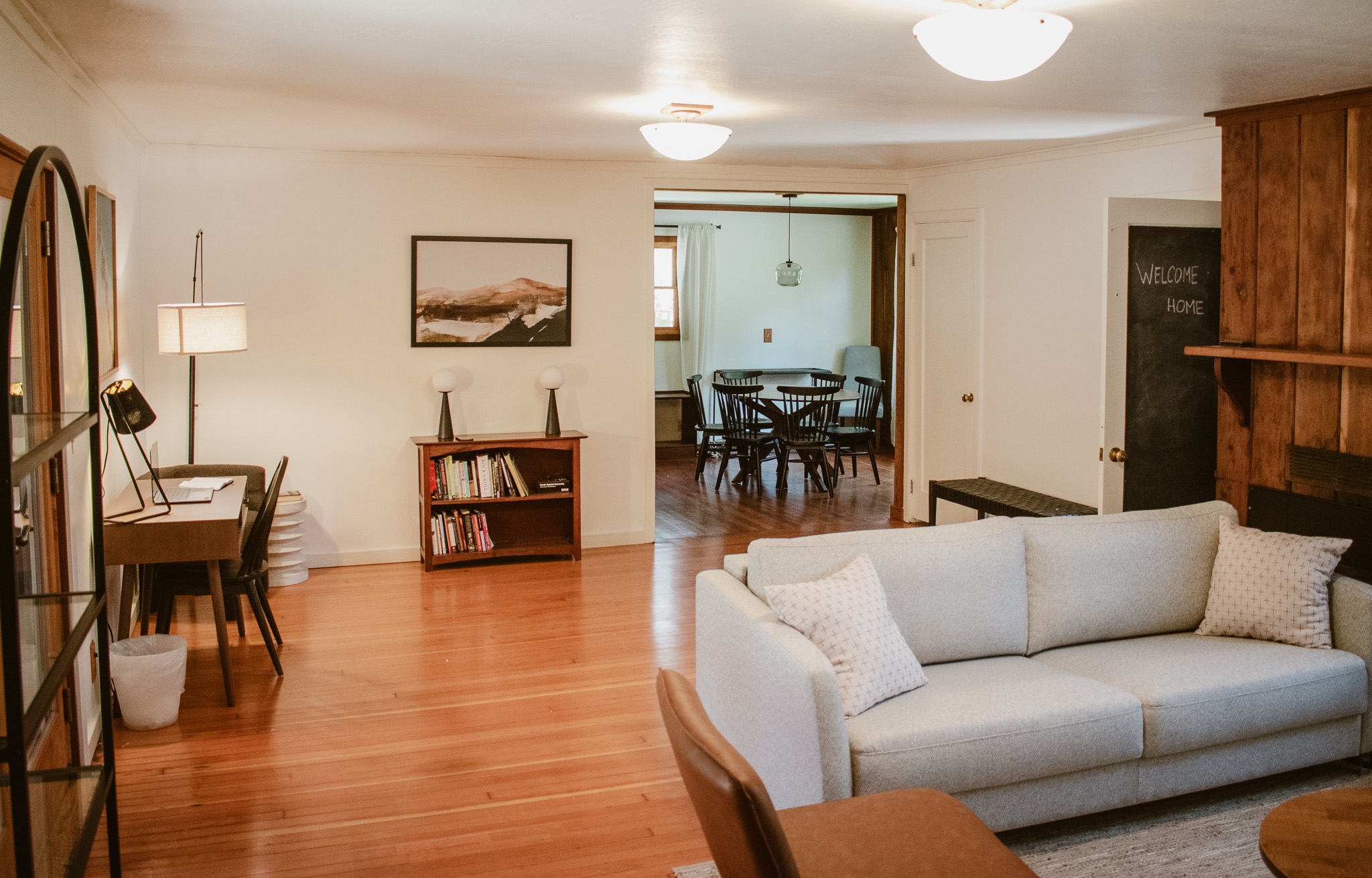 A cozy and inviting living room with a comfortable couch, a workspace, and a view into a bright dining area.