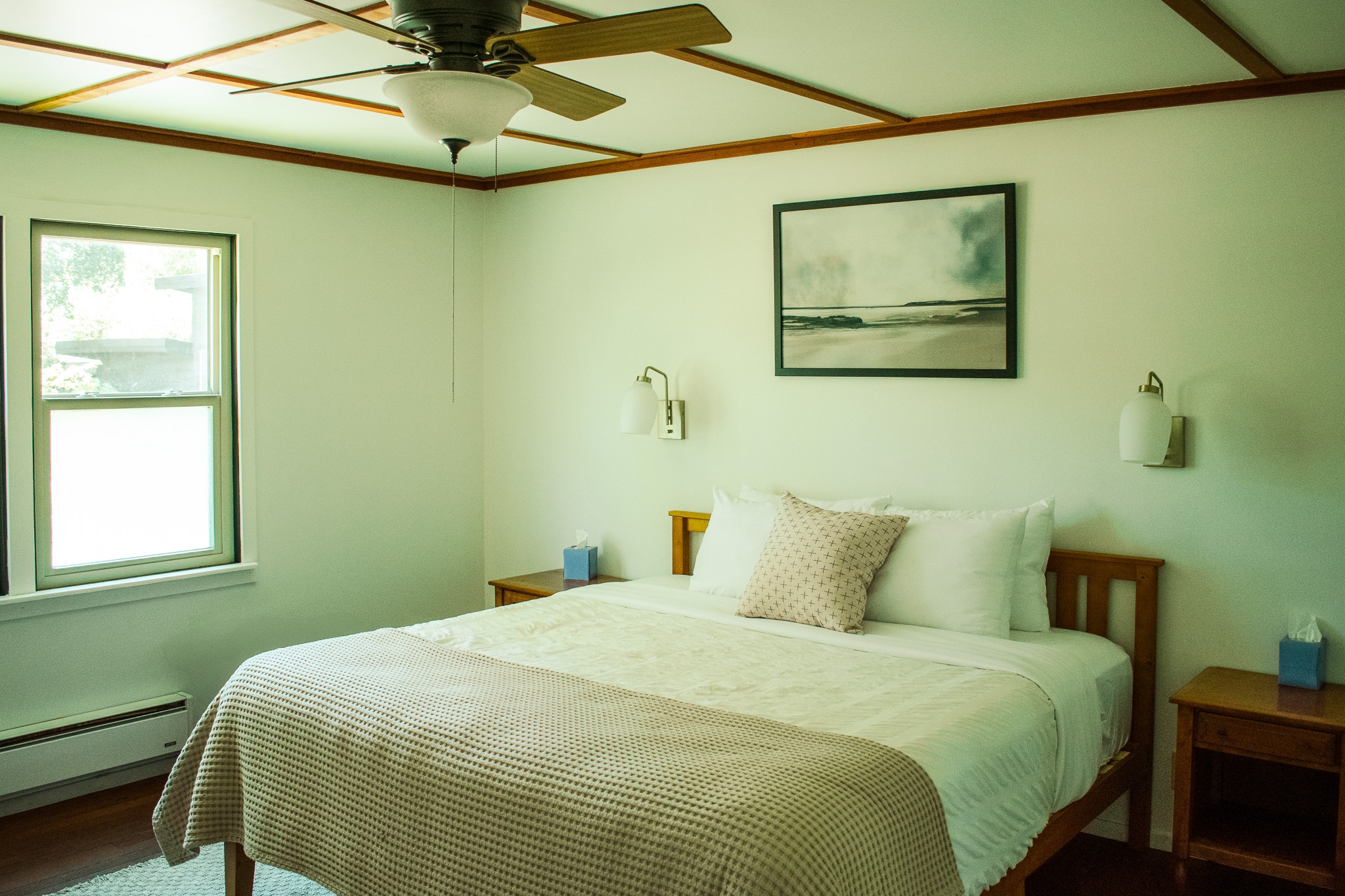 A bedroom with a king-sized bed with white bedding, two nightstands with lamps, a ceiling fan, and a window.