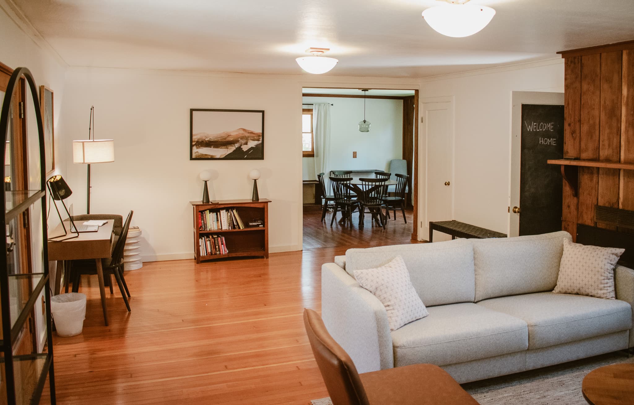 A cozy and inviting living room with a comfortable couch, a workspace, and a view into a bright dining area.