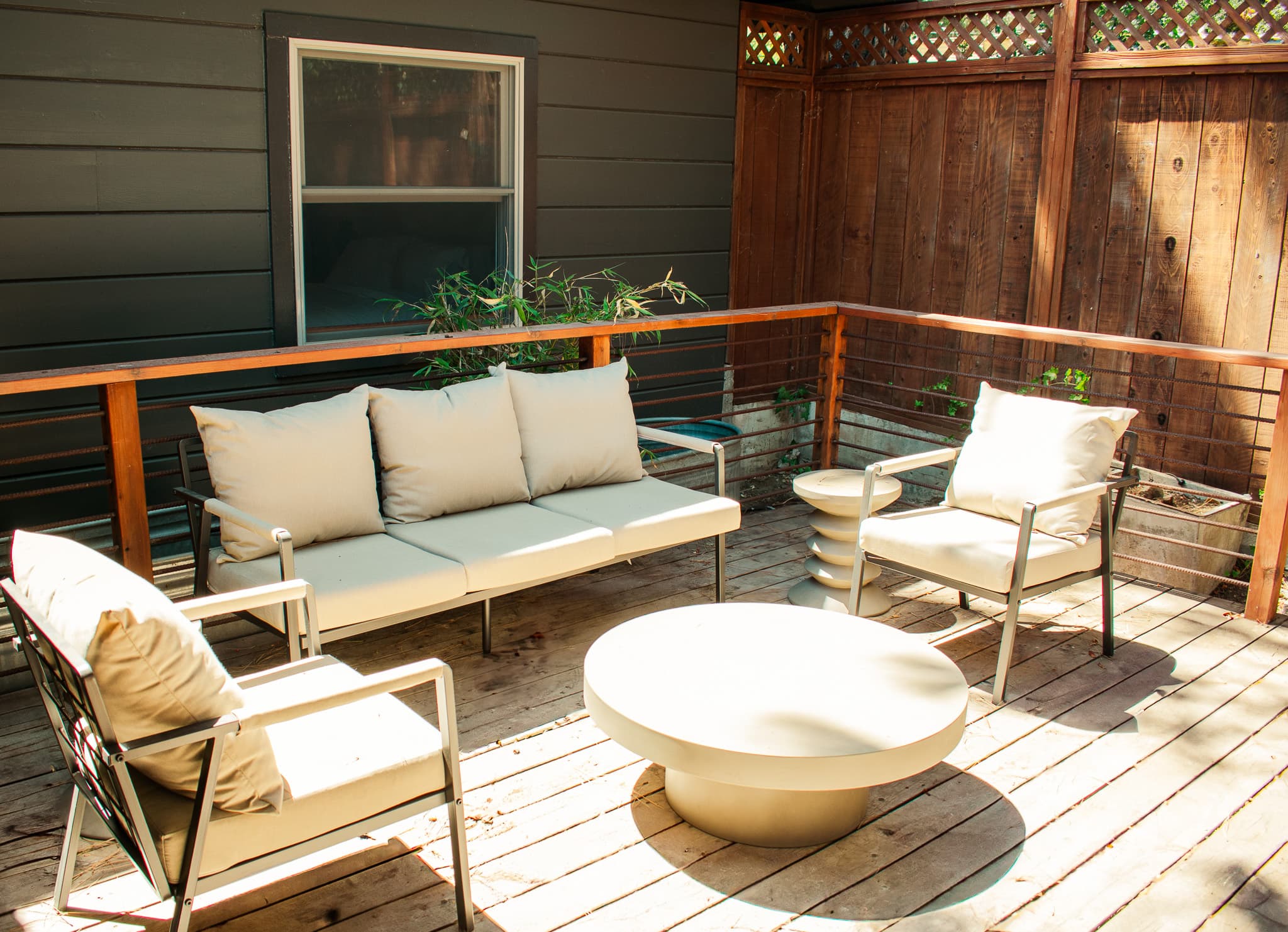 A private patio with a white couch, two armchairs, a round coffee table, and a wooden fence with a lattice top.