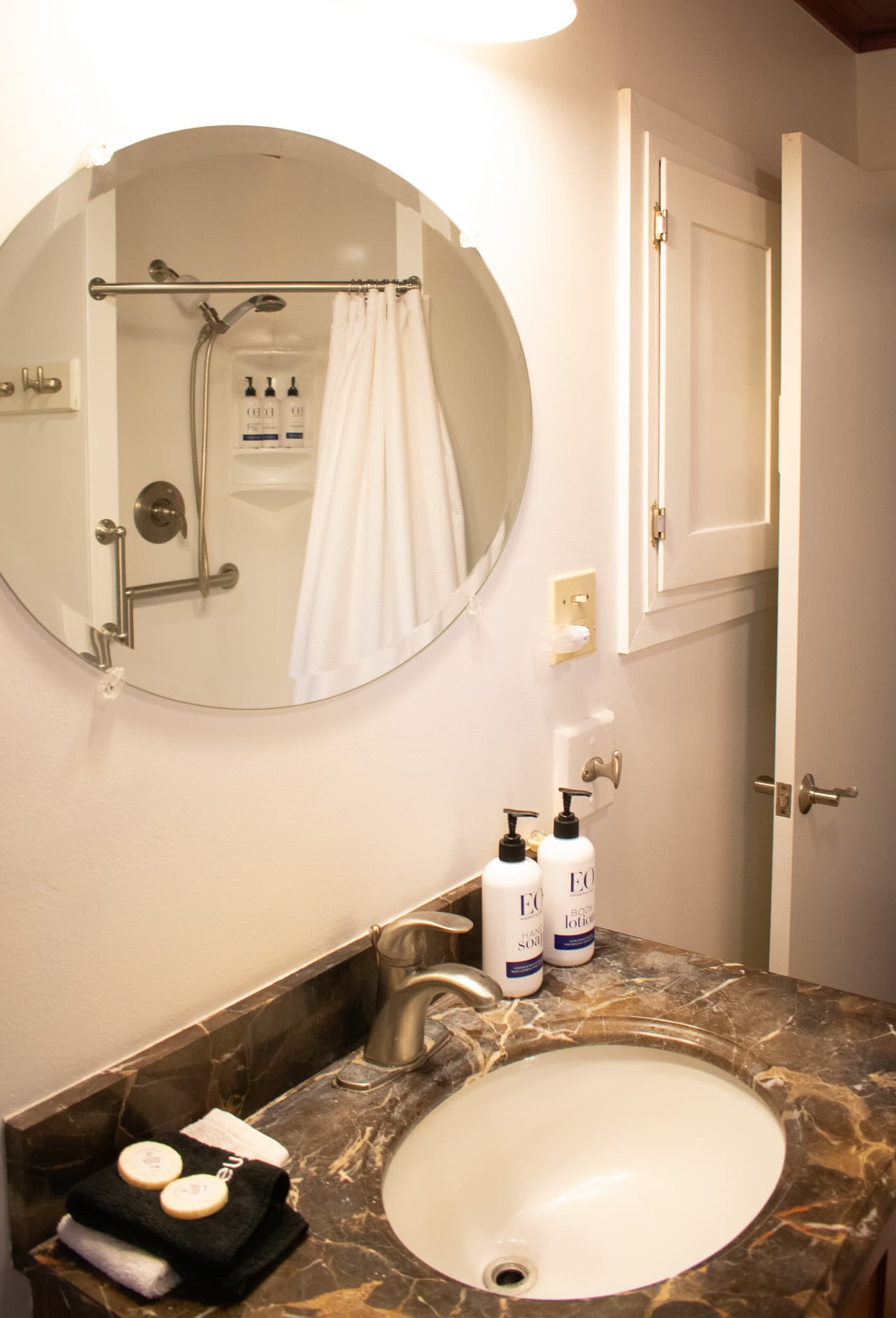 A bathroom with a marble countertop sink, a round mirror, and a shower with a white curtain.